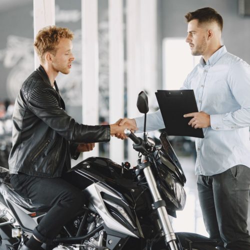 Man choosed motorcycles in moto shop. Guy in a black jacket. Manager with client.